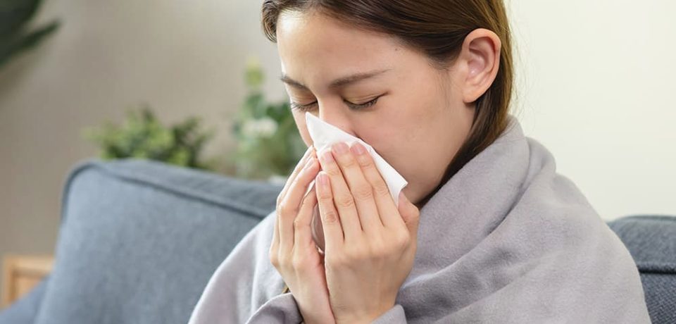 Image of a woman experiencing a cold wrapped in a blanket
