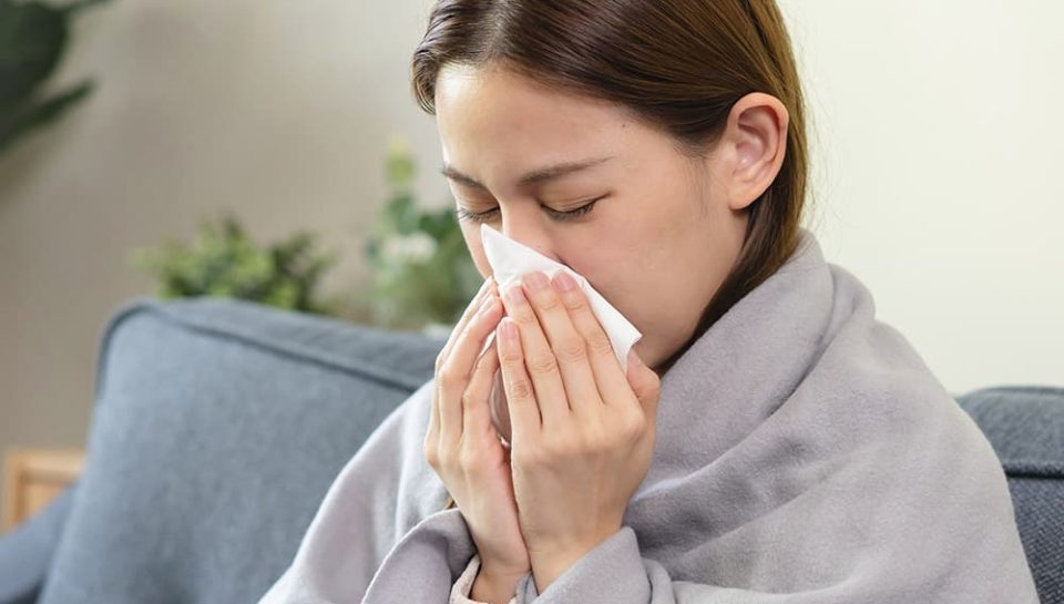 Image of a woman experiencing a cold wrapped in a blanket