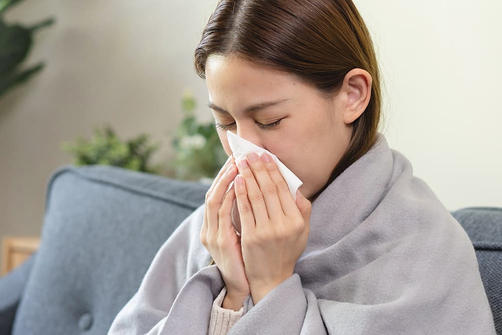 Image of a woman experiencing a cold wrapped in a blanket